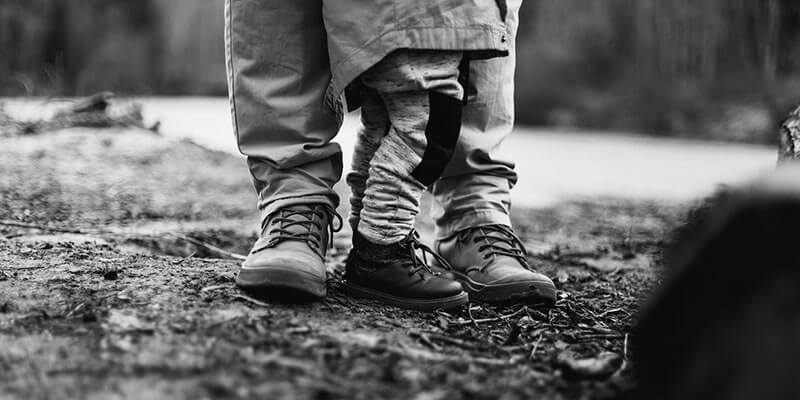 Booted feet of parent and toddler on a woodland path