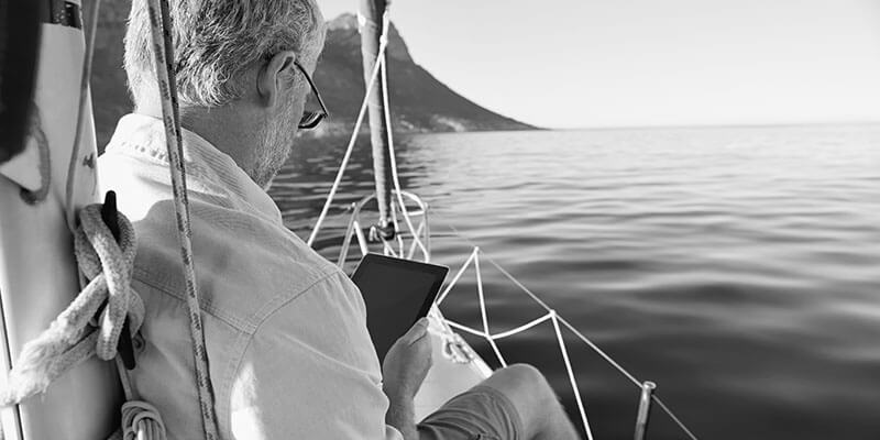 Retired man sat on a yacht looking at a tablet