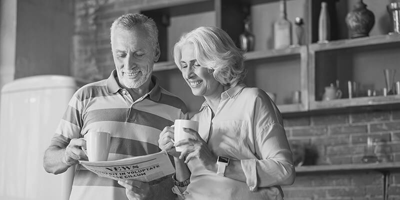 Happy couple holding mugs looking at a newspaper