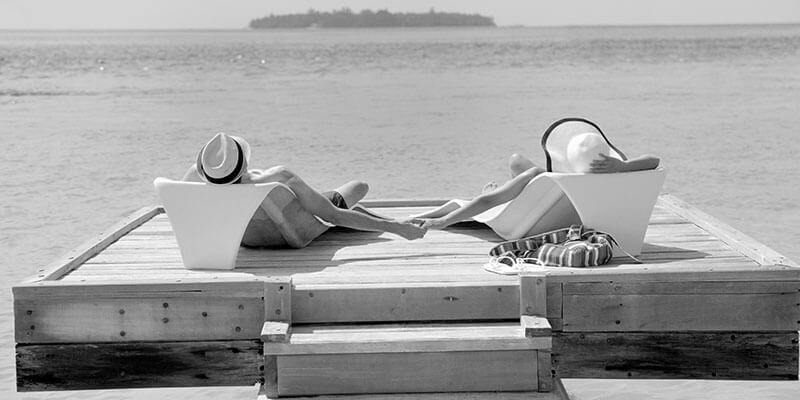 Relaxed couple in sun loungers holding hands overlooking the ocean