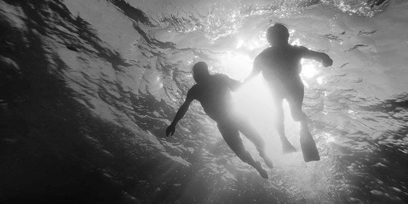 Silhouette off two divers holding hands swimming through the ocean