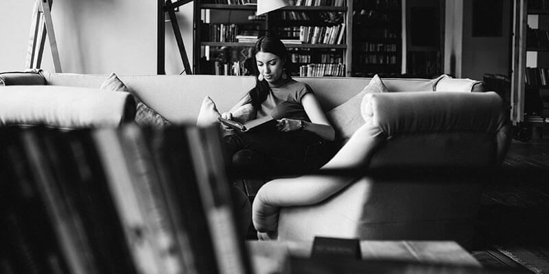 Young woman sat on a sofa reading a large book