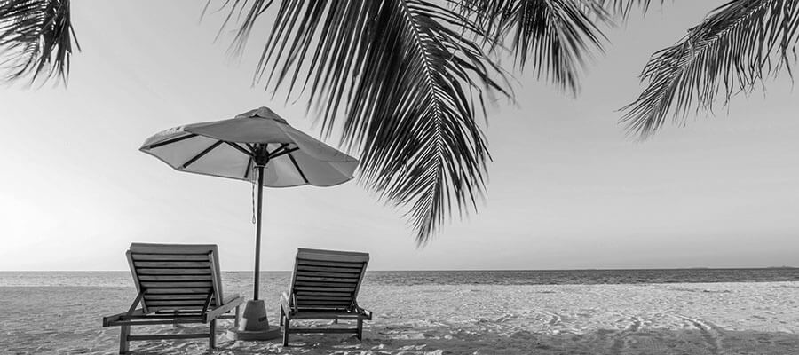 Two empty sun lounges and a parasol on a tropical sandy beach