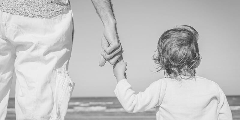 Parent holding hands with a toddler overlooking the ocean